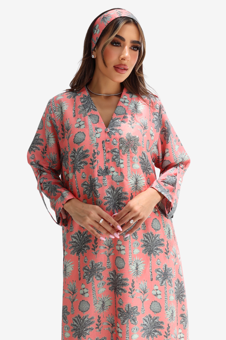 A woman modeling a coral pink long-sleeve tunic dress with a gray botanical and tribal pattern, paired with a matching headband, against a light gray background.