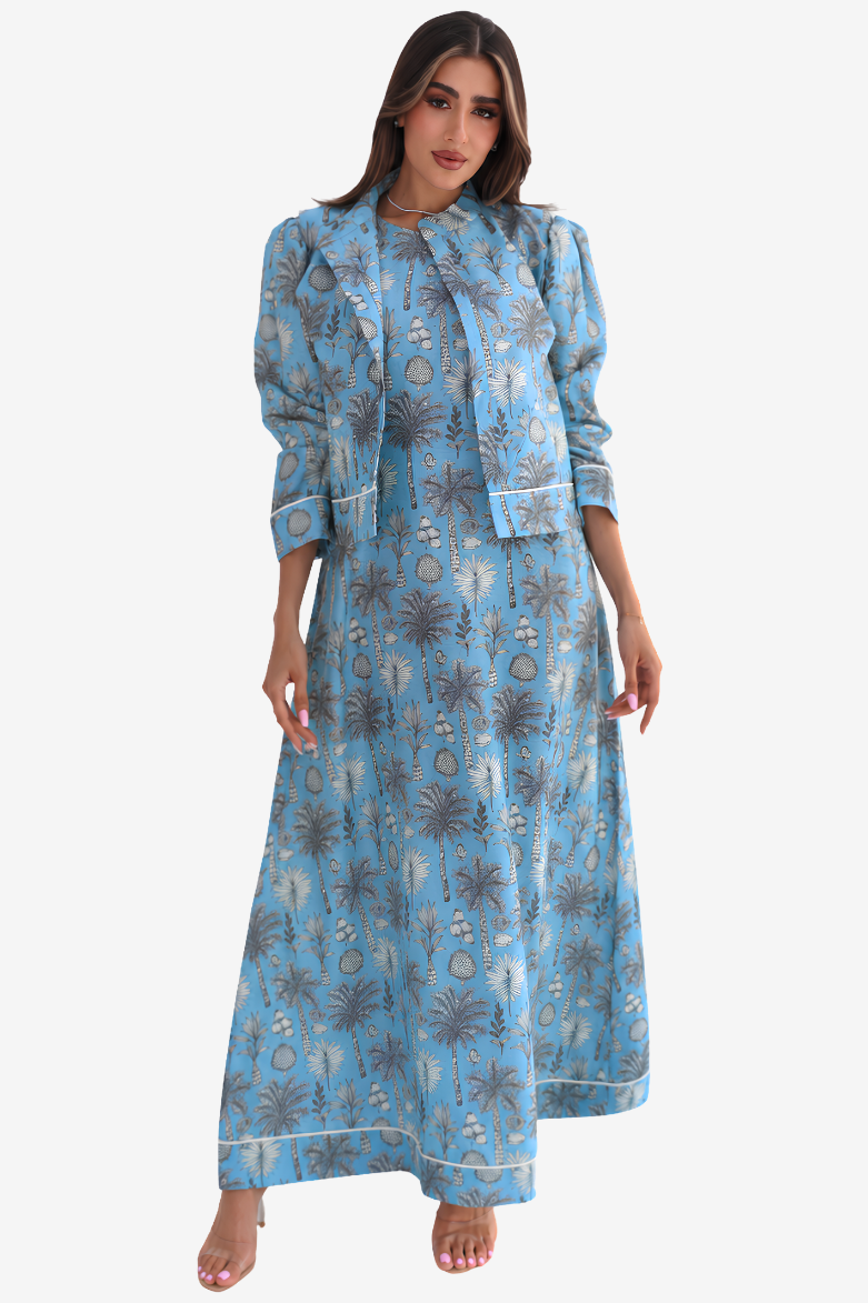 A woman modeling a light blue maxi dress with a gray and white palm tree pattern, shown against a plain light gray background.