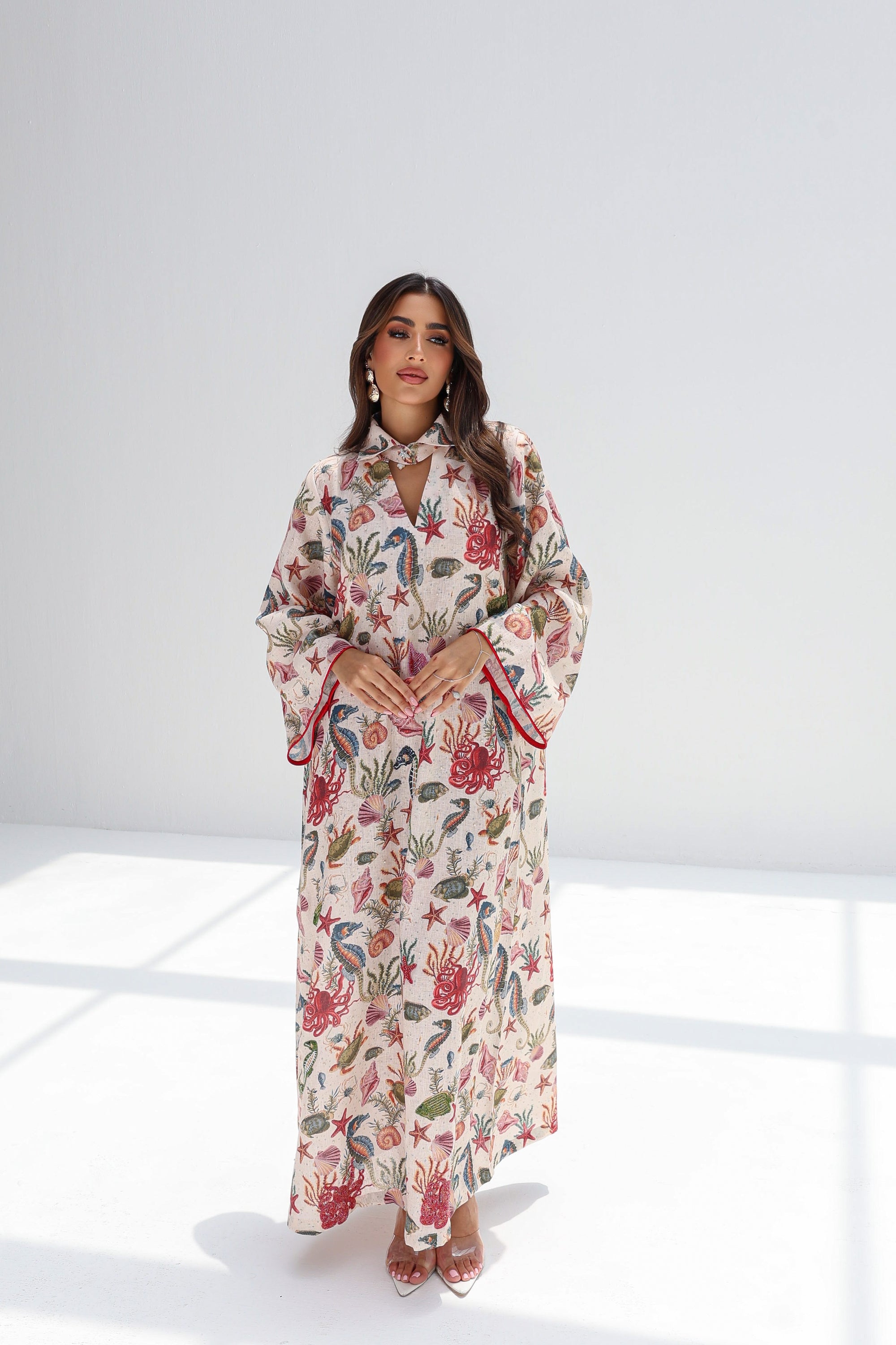Full-length styled view of ivory linen blend jalabiya with coral-toned sleeve and hem borders
