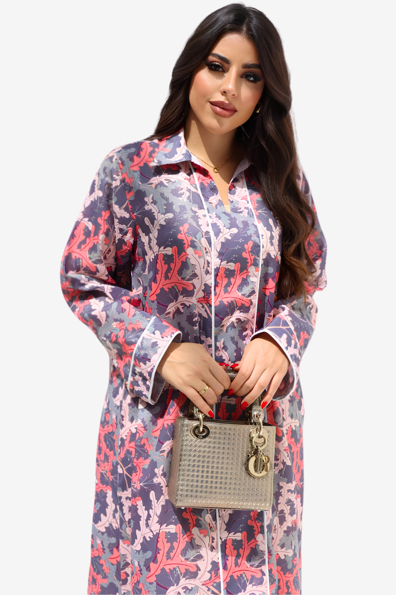 A woman modeling a long-sleeve button-up shirt dress with a purple, pink, and white abstract pattern, holding a small gray handbag against a light gray background.