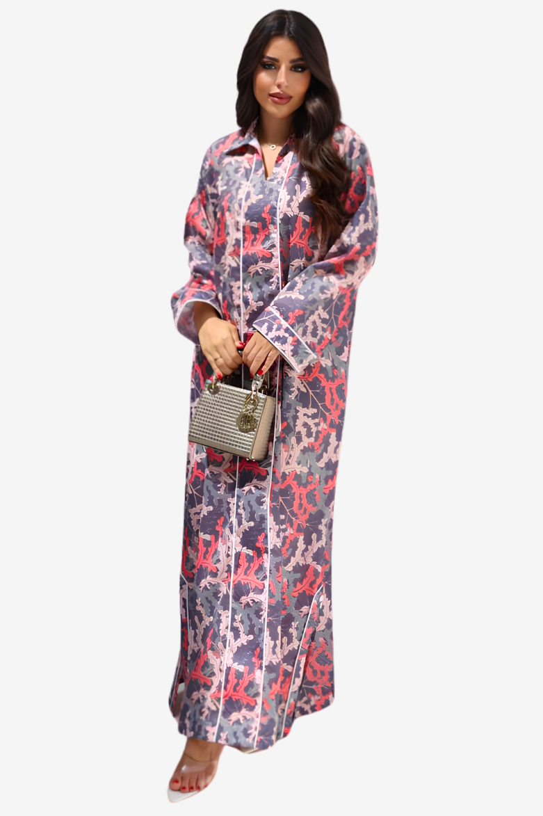 A woman modeling a long-sleeved, collared maxi dress with a pink, purple, and white abstract pattern, holding a small striped handbag against a light gray background.