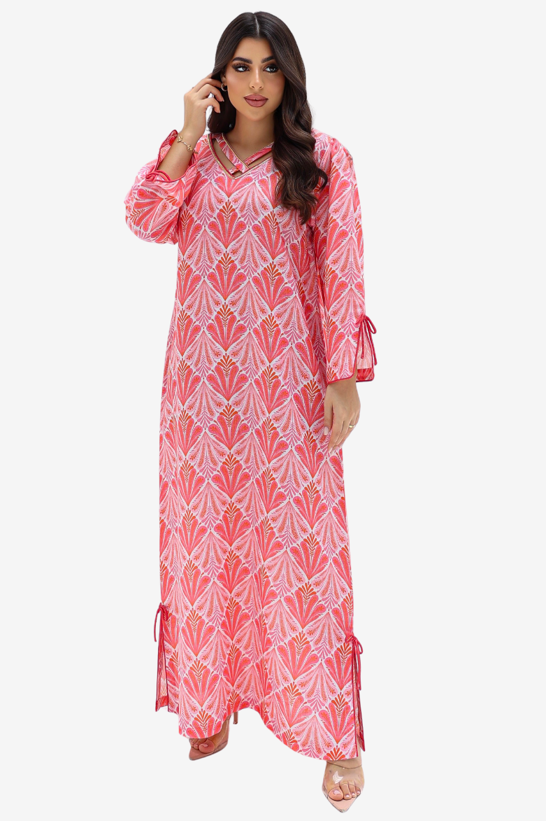 A woman modeling a long pink and white printed kaftan dress with geometric patterns, 3/4 sleeves, and side tie details, set against a plain light gray background.