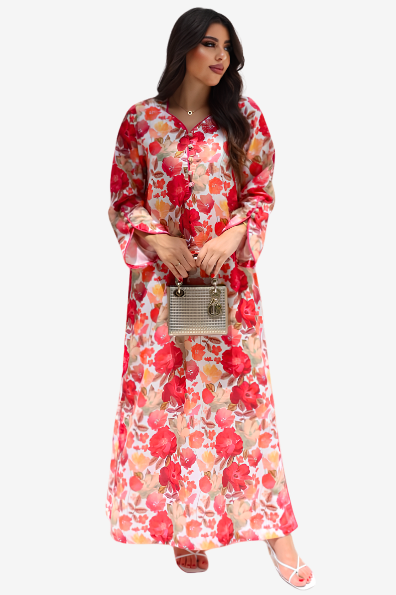 A woman modeling a long-sleeved maxi dress with a vibrant red, pink, and orange floral print on a white base, holding a small metallic handbag against a light gray background.