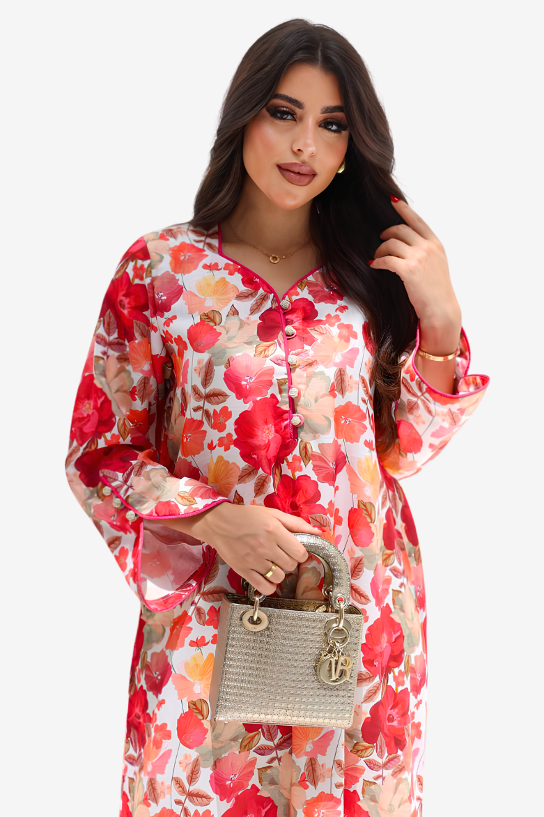 A woman modeling a long-sleeve floral dress with red, pink, and orange flowers on a white background, holding a small gray handbag against a light gray studio backdrop.