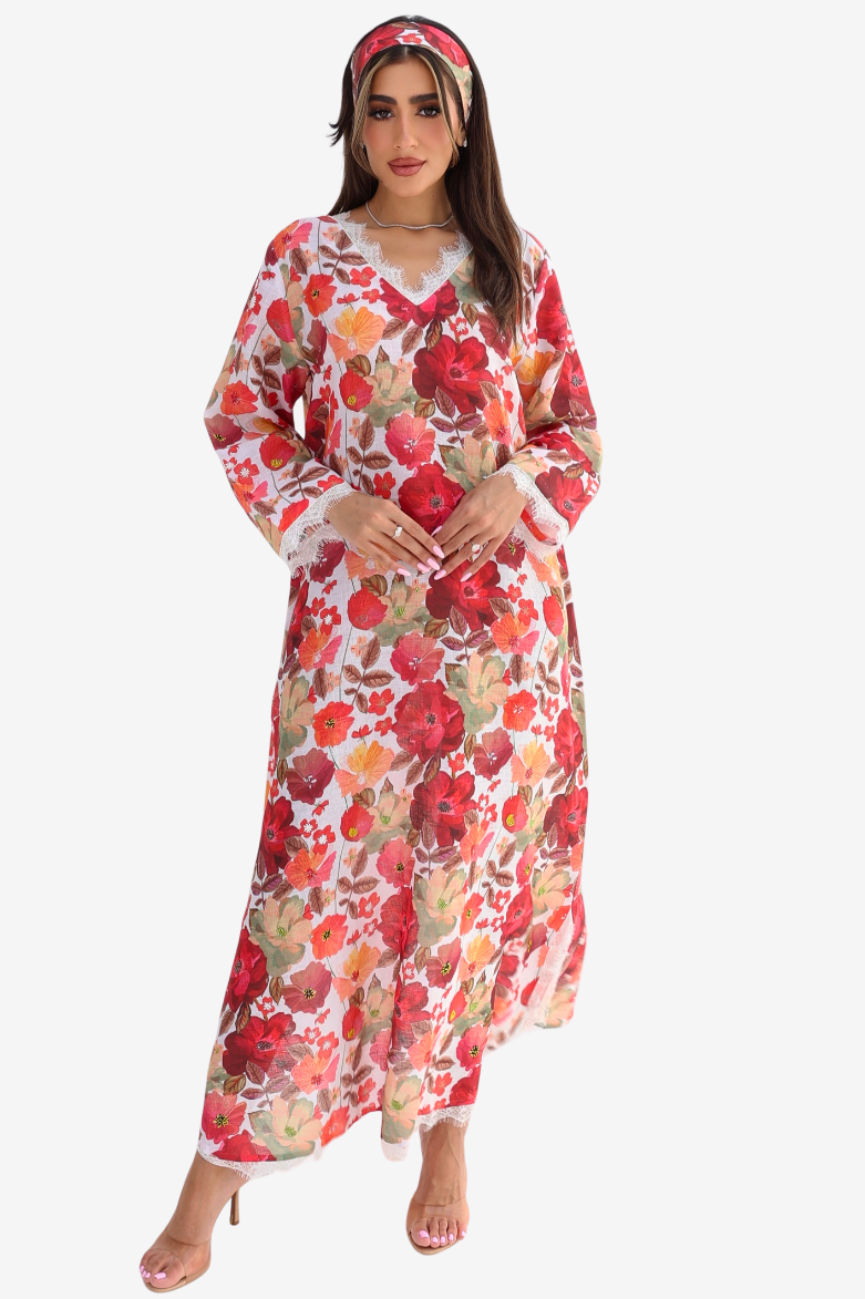 A woman modeling a long-sleeved, V-neck maxi dress with a vibrant red, pink, and orange floral pattern on a white base, paired with a matching floral headband, set against a plain light gray background.