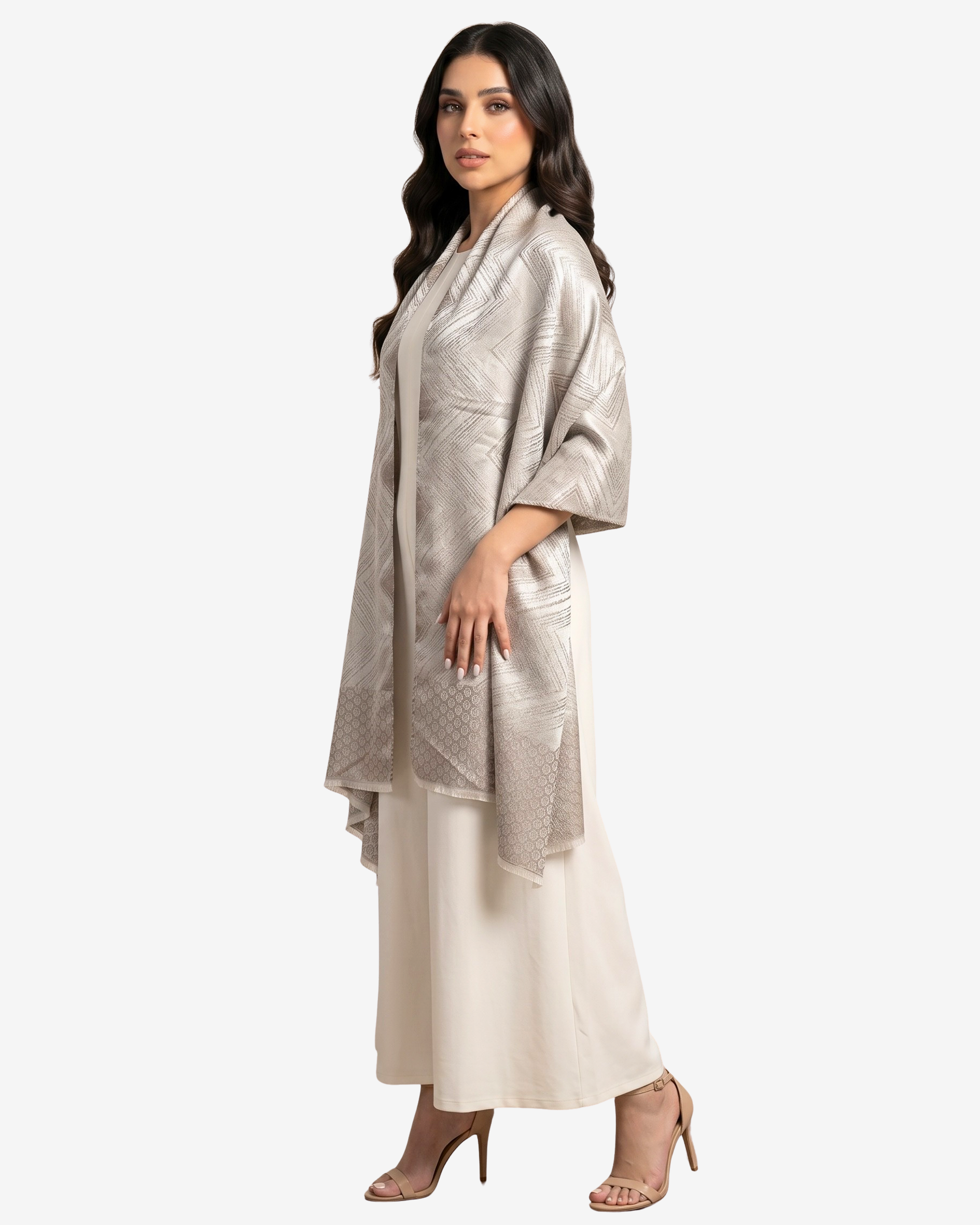 A woman modeling a shimmering champagne metallic shawl draped over a cream-colored dress, set against a plain light gray studio background.