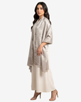 A woman modeling a shimmering champagne metallic shawl draped over a cream-colored dress, set against a plain light gray studio background.
