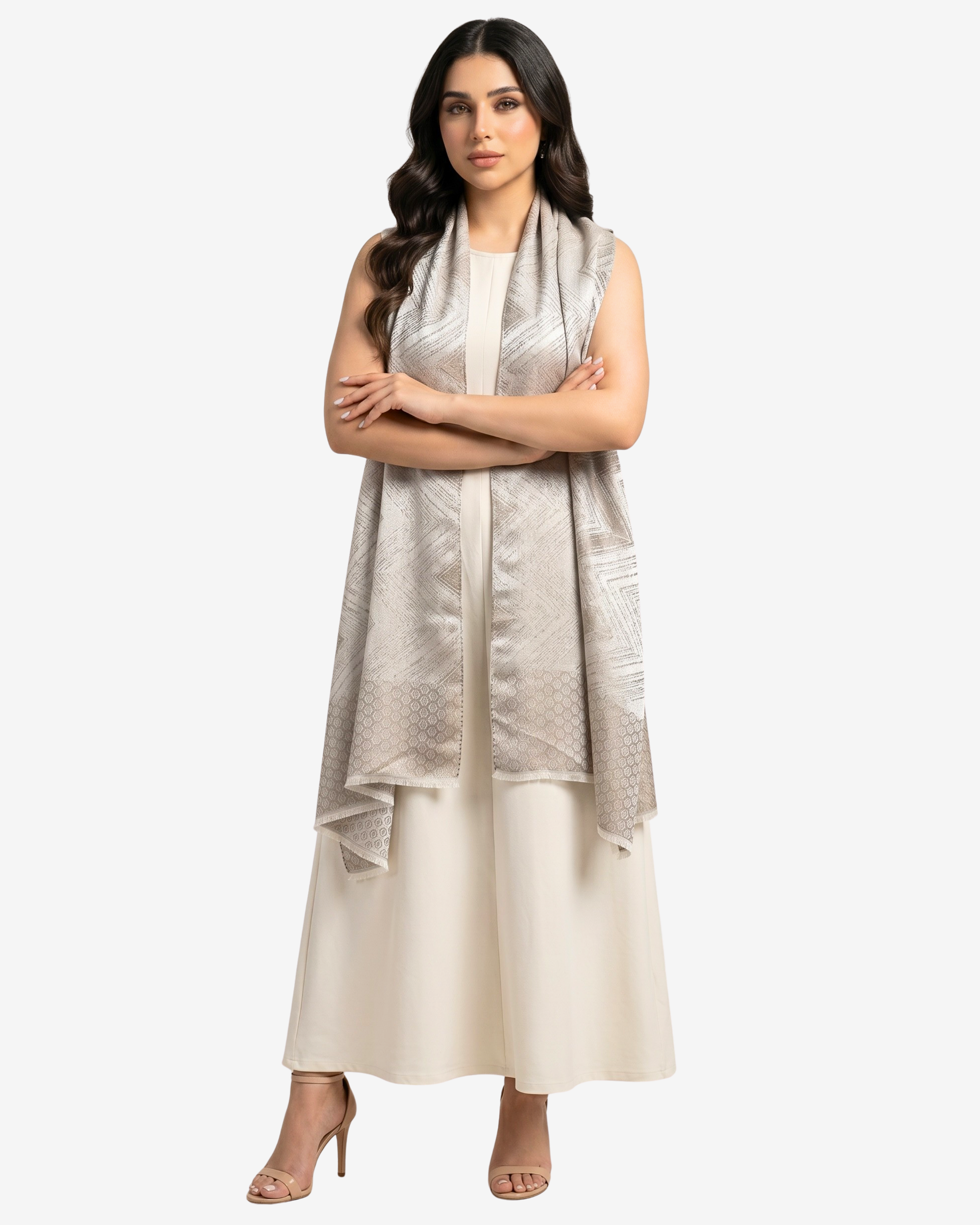 A woman modeling a sleeveless light beige and silver patterned shawl draped over a cream-colored dress, standing against a solid light gray background.