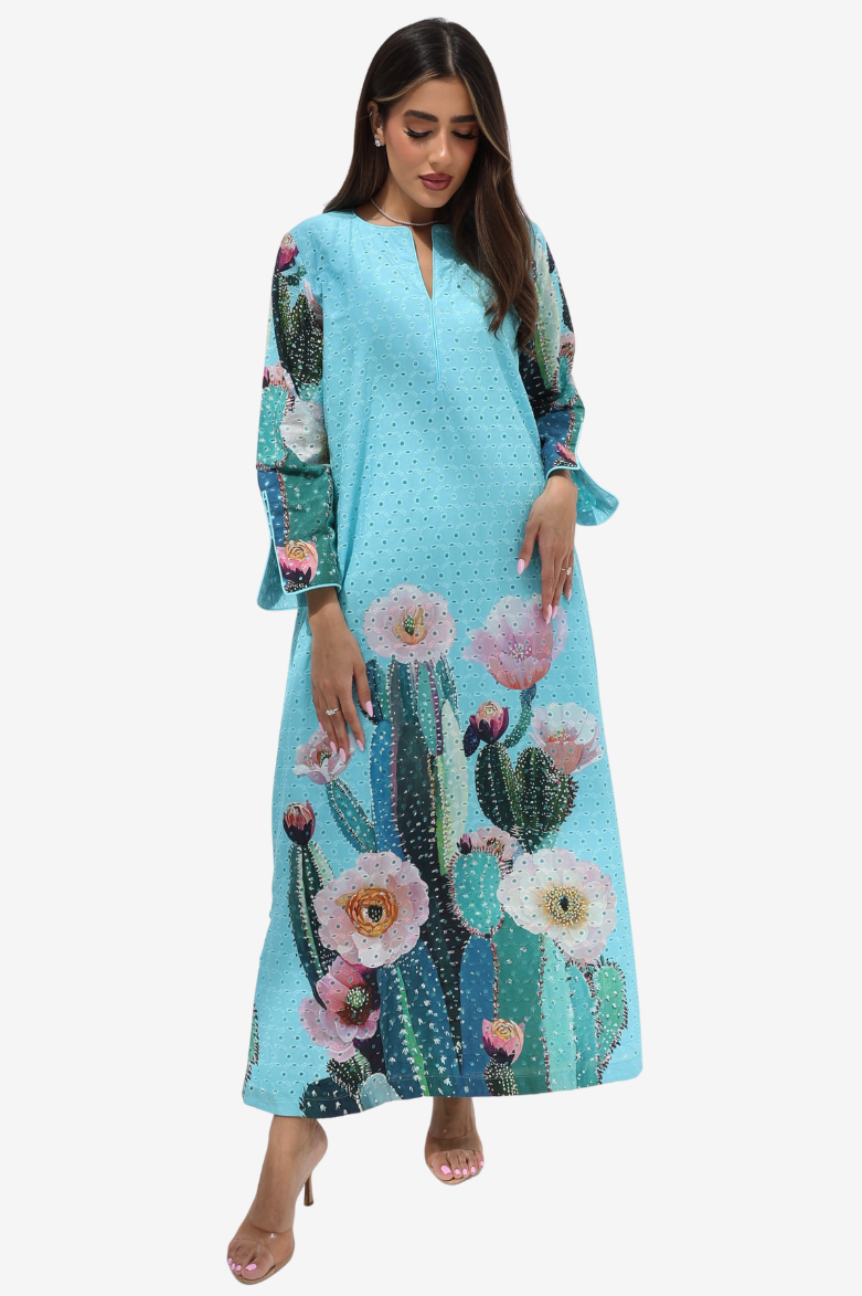 A woman modeling a light blue maxi dress with a cactus and pink flower print, set against a plain light gray background.