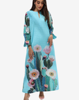 A woman modeling a light blue maxi dress with a cactus and pink flower print, set against a plain light gray background.
