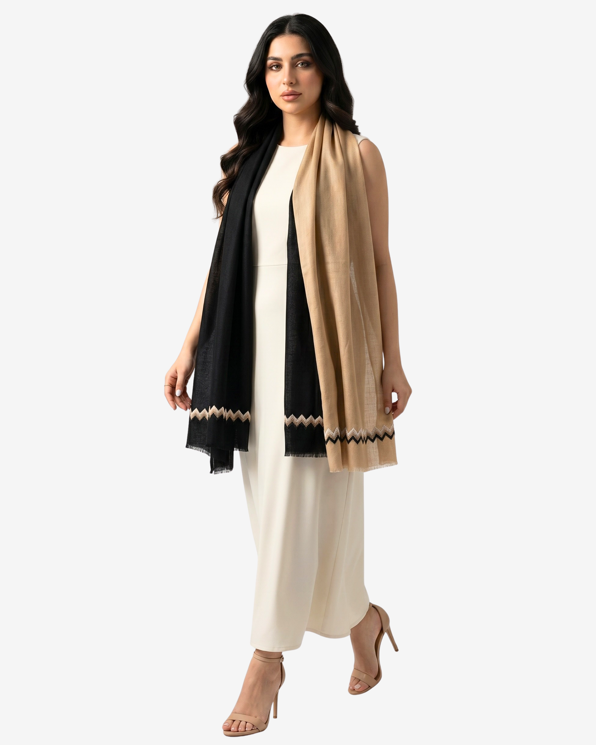 A woman modeling a long beige and black shawl with a geometric patterned border, worn over a cream-colored dress against a light gray background.