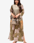 A woman modeling a long-sleeved, knee-length kurta with a split leg, featuring a beige and olive green base with a floral pattern in dusty pink and mustard yellow. She is holding a matching beige handbag and wearing beige sandals against a plain light gray background.