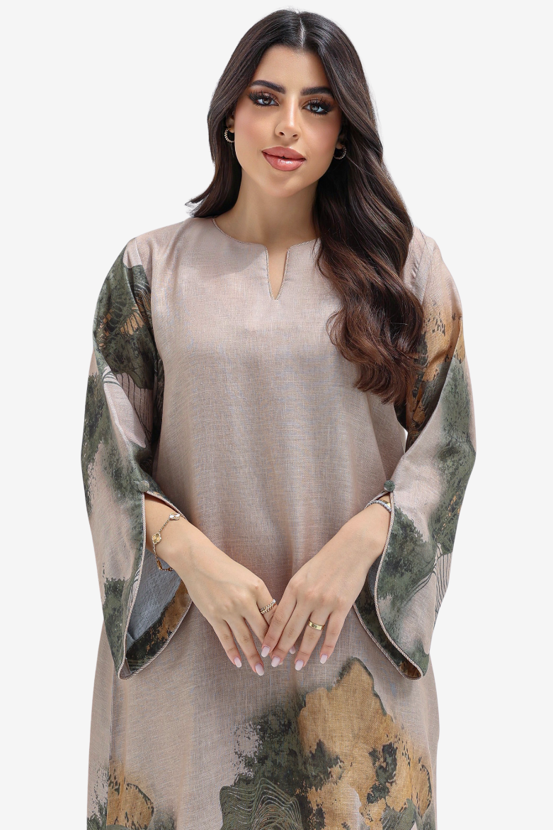 A woman modeling a loose, long-sleeved tunic dress with a beige base and green, brown, and gold abstract watercolor-style print on the sleeves and hem, set against a plain light gray background.