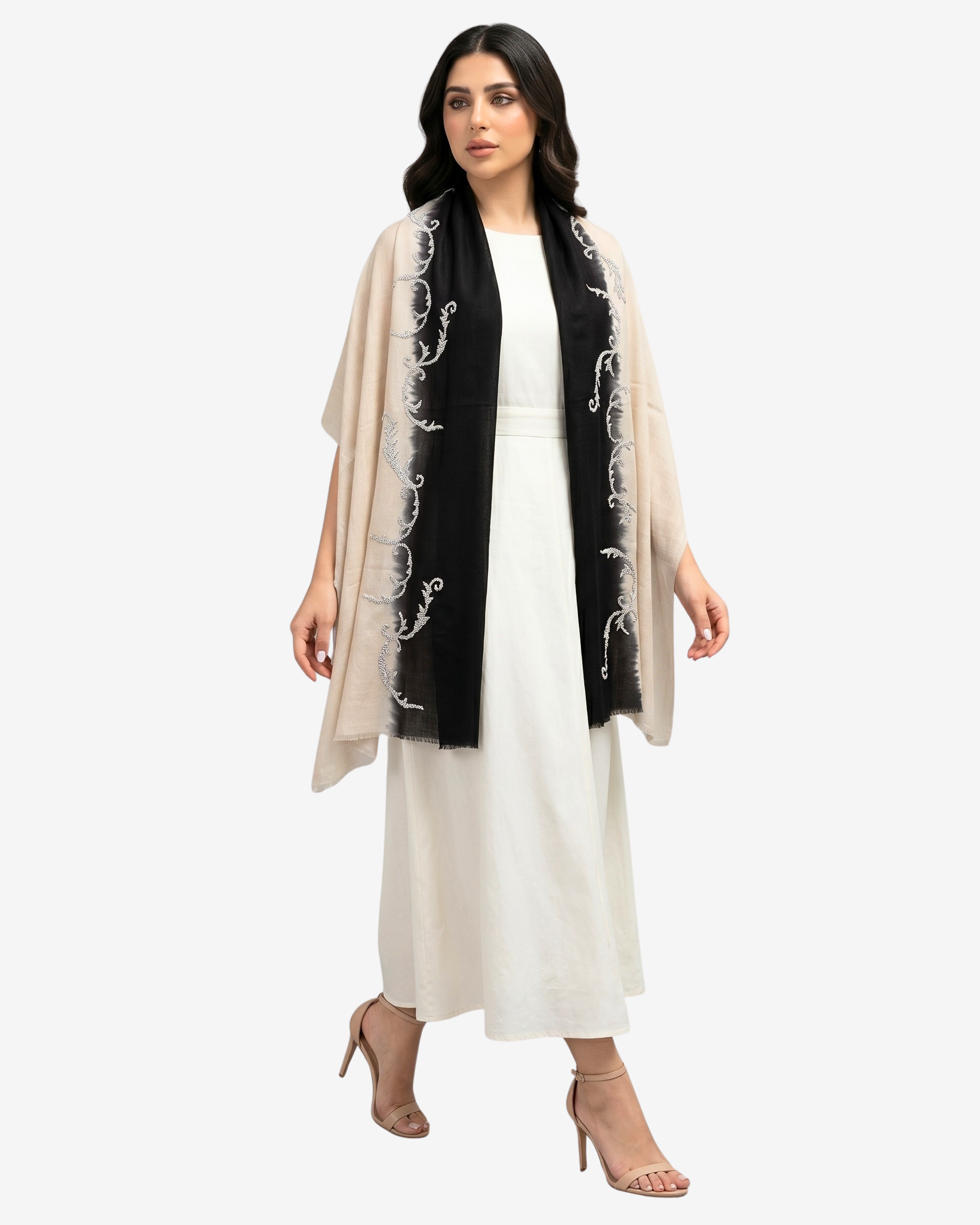 A woman modeling a black scarf with white floral embroidery draped over a white dress, against a light gray studio background.