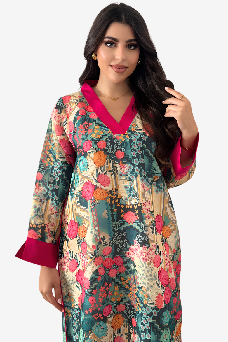 A woman modeling a long-sleeved floral print tunic with a vibrant pink V-neck and cuffs, set against a plain light gray background.