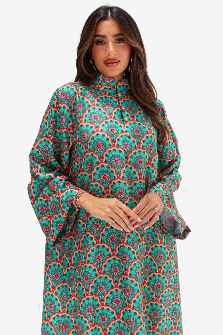 A woman modeling a long-sleeved high-neck tunic dress with a vibrant green, red, and orange mandala pattern against a light gray studio background.