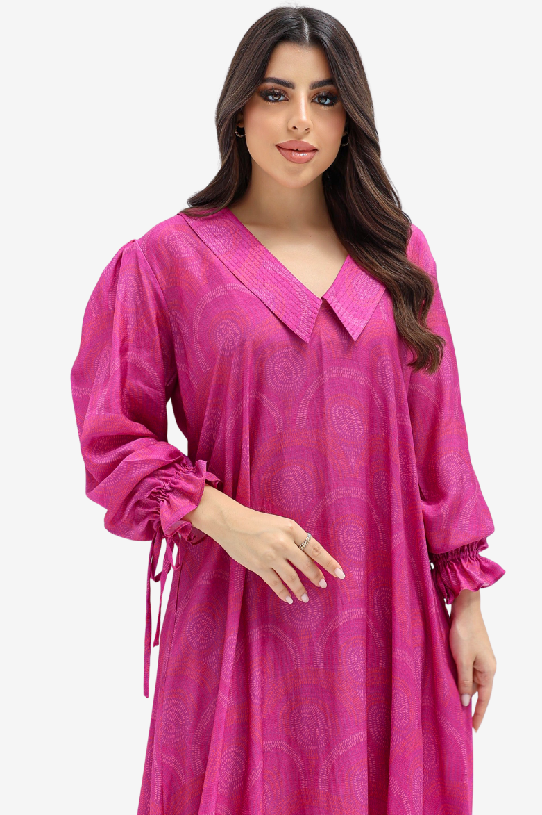 A woman modeling a bright pink long-sleeve tunic dress with a V-neck, subtle tonal paisley pattern, and gathered ruffled cuffs, set against a plain light gray background.
