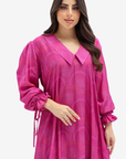 A woman modeling a bright pink long-sleeve tunic dress with a V-neck, subtle tonal paisley pattern, and gathered ruffled cuffs, set against a plain light gray background.