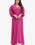 A woman modeling a long magenta pink kaftan dress with a V-neck, long sleeves, and a subtle circular jacquard pattern, set against a plain light gray background.