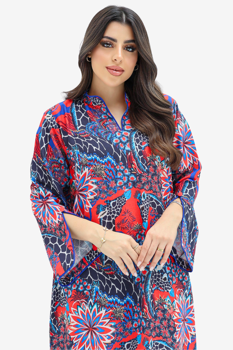 A woman modeling a vibrant, multicolored kaftan dress with a red, blue, and black floral pattern, set against a plain light gray background.