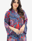 A woman modeling a vibrant, multicolored kaftan dress with a red, blue, and black floral pattern, set against a plain light gray background.