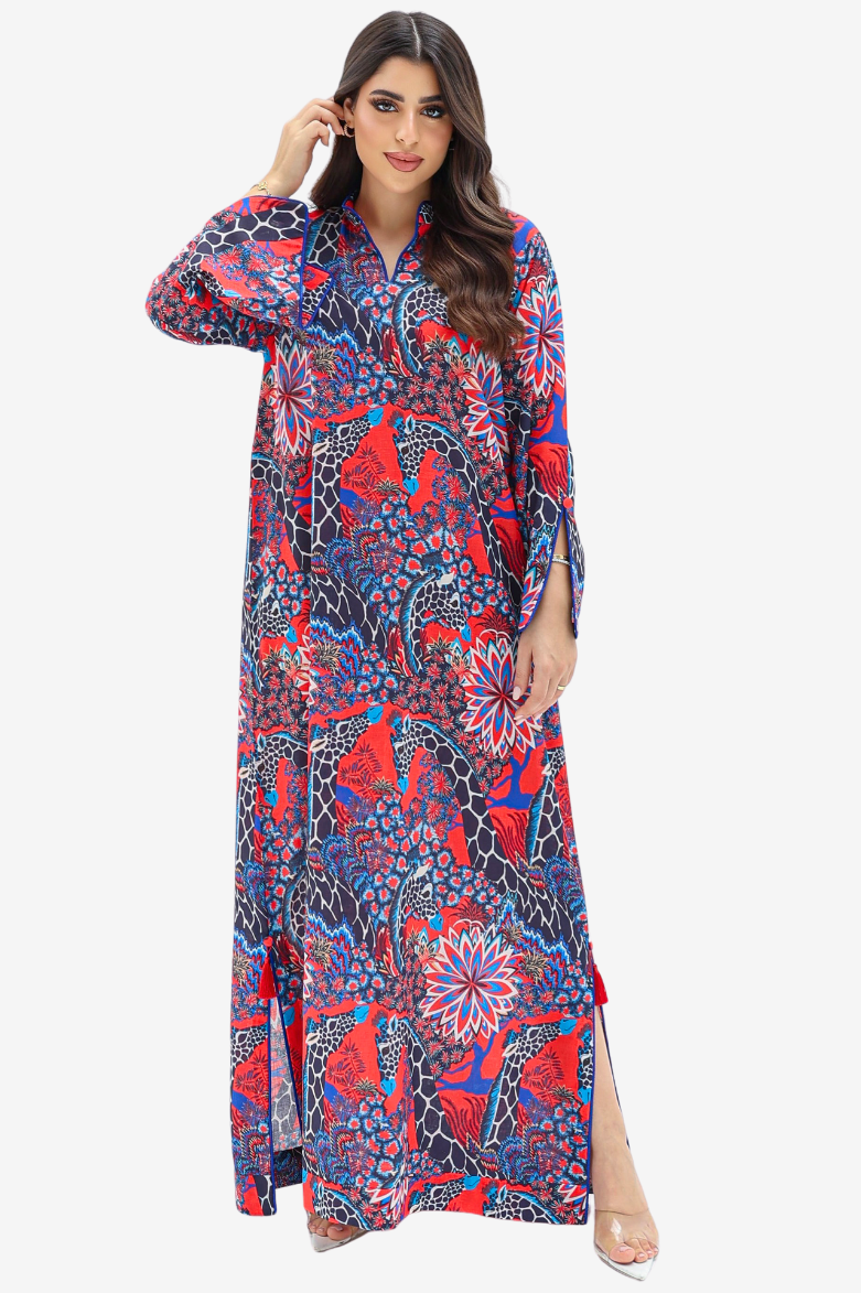 A woman modeling a long-sleeved, floor-length abaya dress with a vibrant red, blue, and black paisley pattern, set against a plain light gray background.
