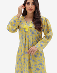 A woman modeling a yellow long-sleeve tunic dress with a blue floral print and yellow tassel tie details at the neckline, set against a plain light gray background.