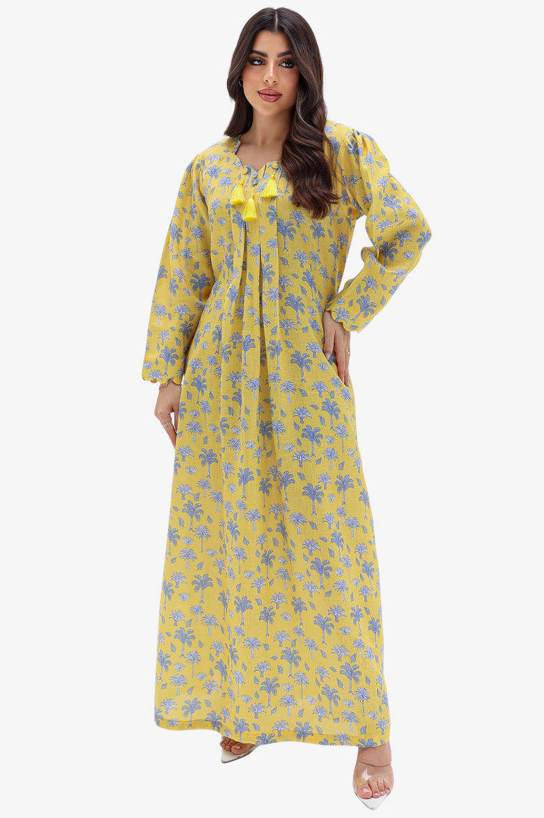 A woman modeling a long yellow maxi dress with a blue floral pattern and a matching yellow bow at the neckline, set against a plain light gray background.