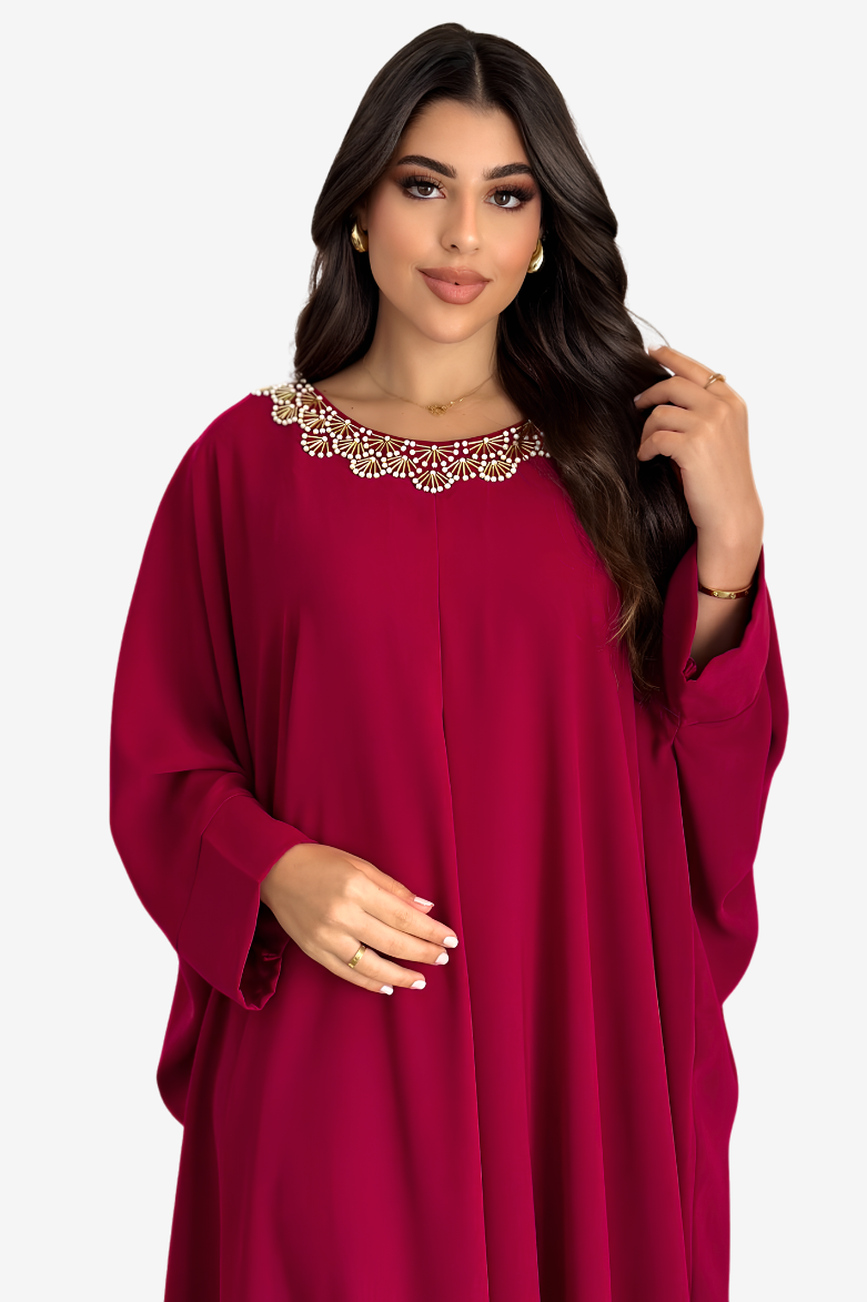 A woman modeling a loose, long-sleeved magenta dress with a decorative beaded neckline, set against a plain light gray background.
