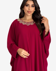A woman modeling a loose, long-sleeved magenta dress with a decorative beaded neckline, set against a plain light gray background.