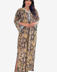 A woman modeling a long kaftan dress with a beige, brown, and yellow leopard print pattern and gray trim, set against a plain light gray background.