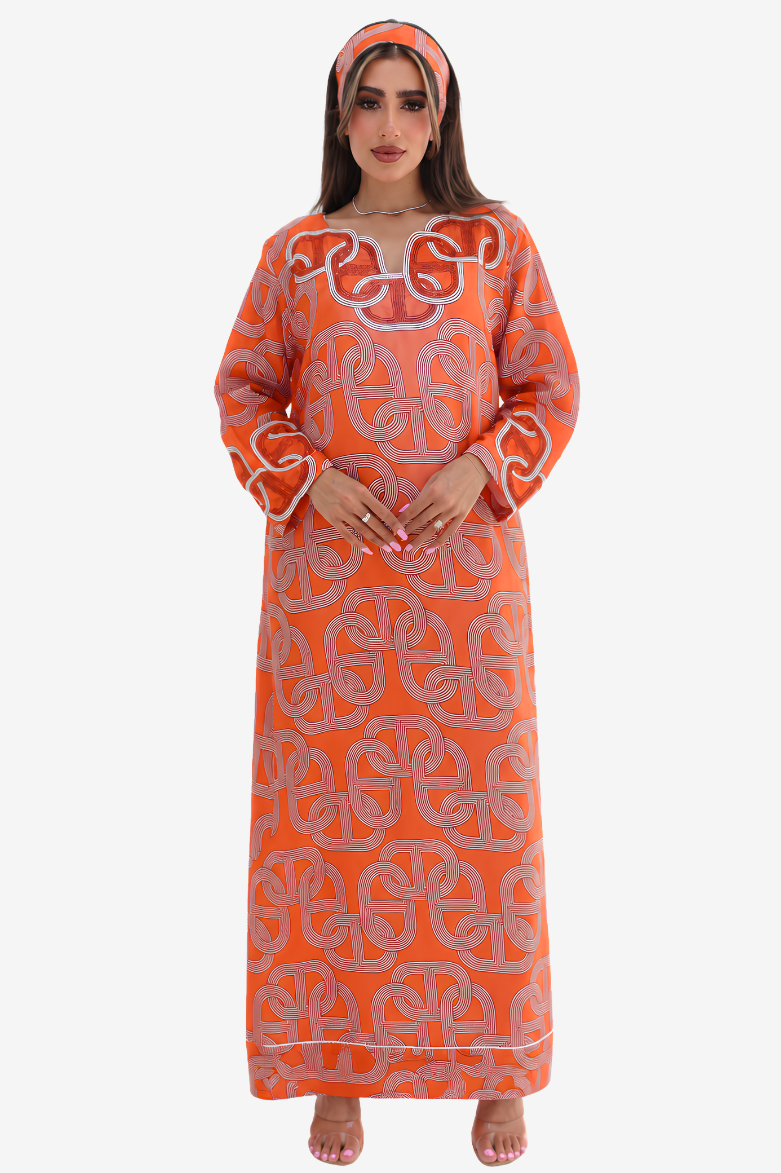 A woman modeling a long-sleeved orange kaftan dress with a light pink geometric pattern and a matching headscarf, set against a plain light gray background.