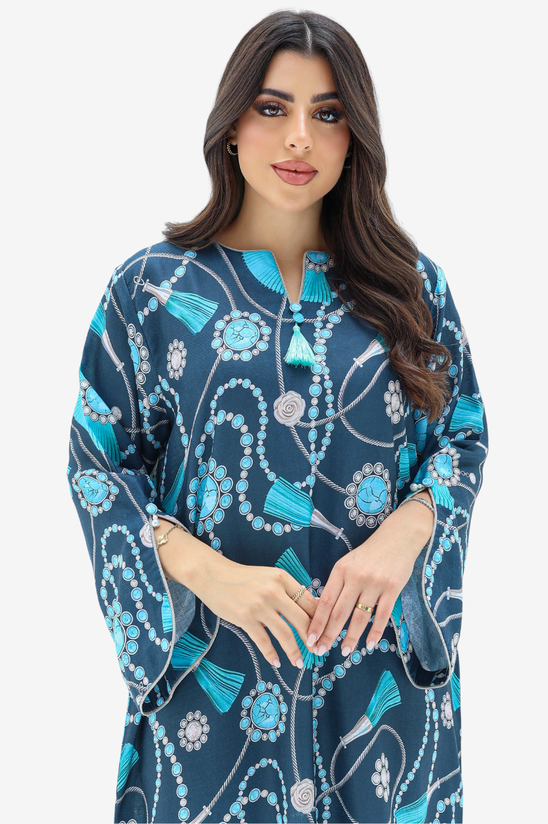 A woman modeling a navy blue kaftan dress with a vibrant turquoise, white, and gray beaded and tassel print against a plain light gray background.