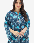 A woman modeling a navy blue kaftan dress with a vibrant turquoise, white, and gray beaded and tassel print against a plain light gray background.