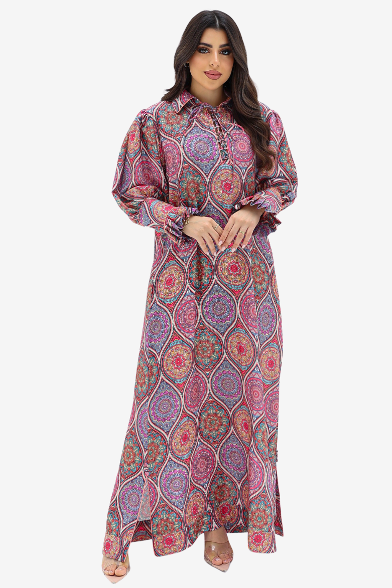 A woman modeling a long-sleeved, collared maxi dress with a vibrant pink, purple, and orange paisley pattern against a plain light gray background.