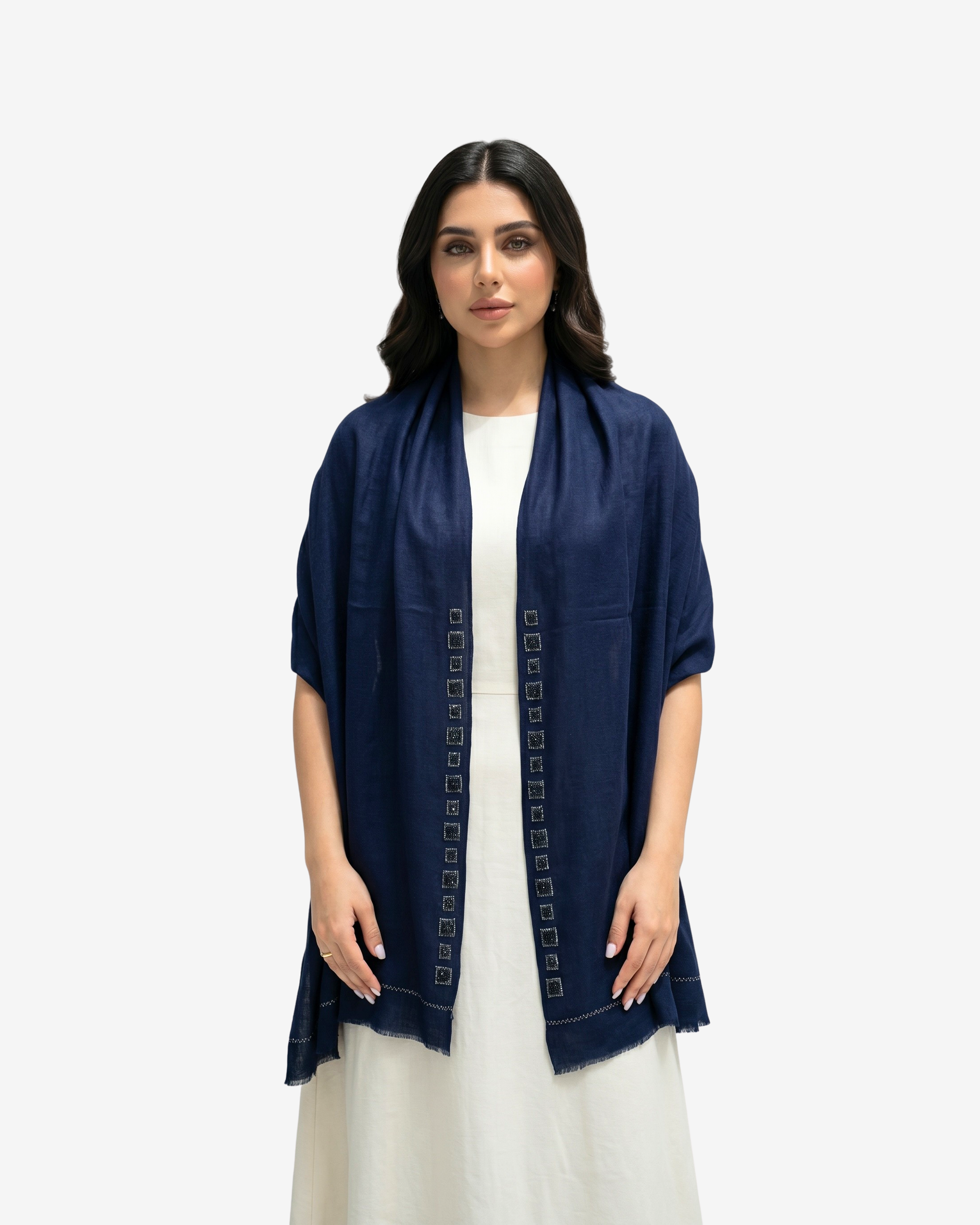 A woman modeling a navy blue open-front shawl or lightweight jacket with decorative geometric embroidery down the front, worn over a white dress against a light gray studio background.