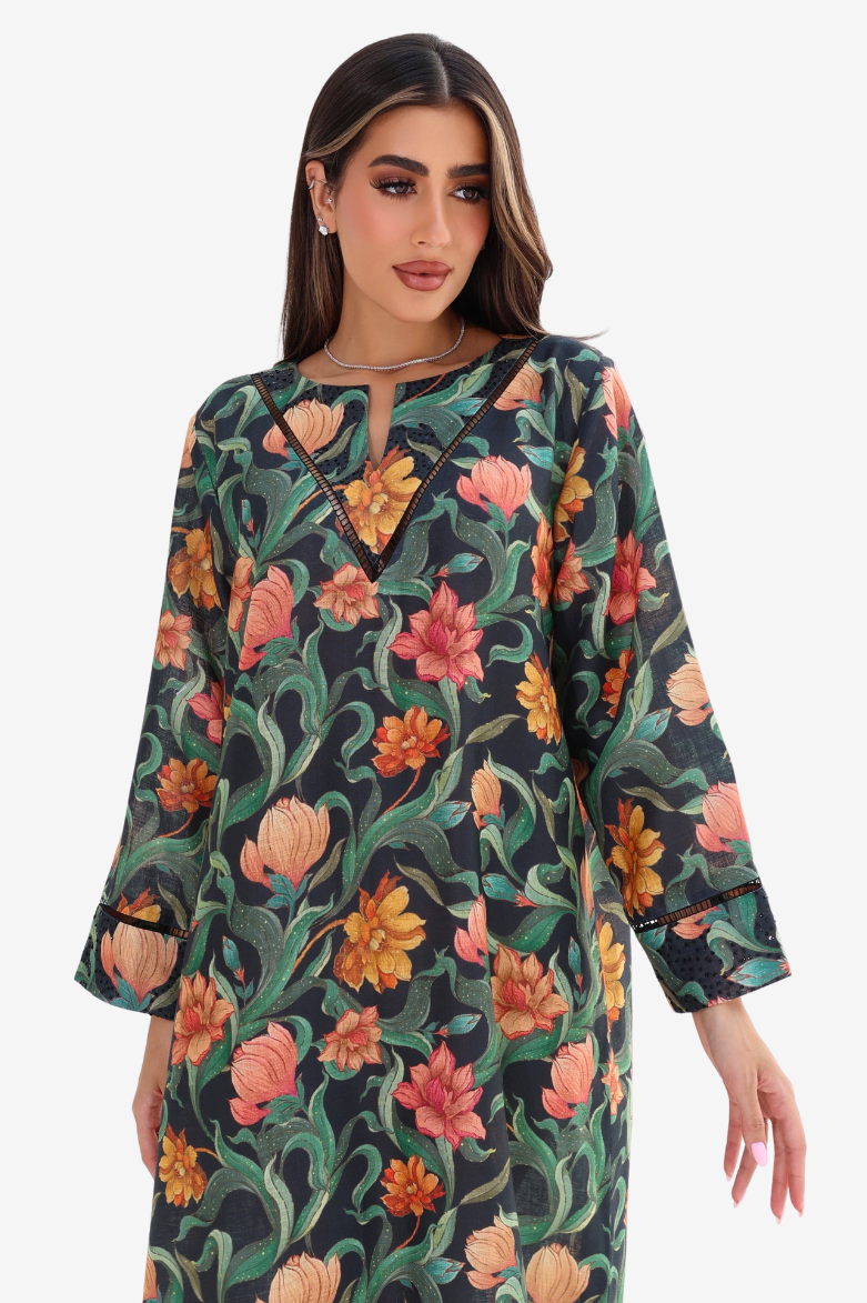 A woman wearing a long-sleeve floral print tunic dress with a keyhole neckline and black trim, set against a plain light gray background.