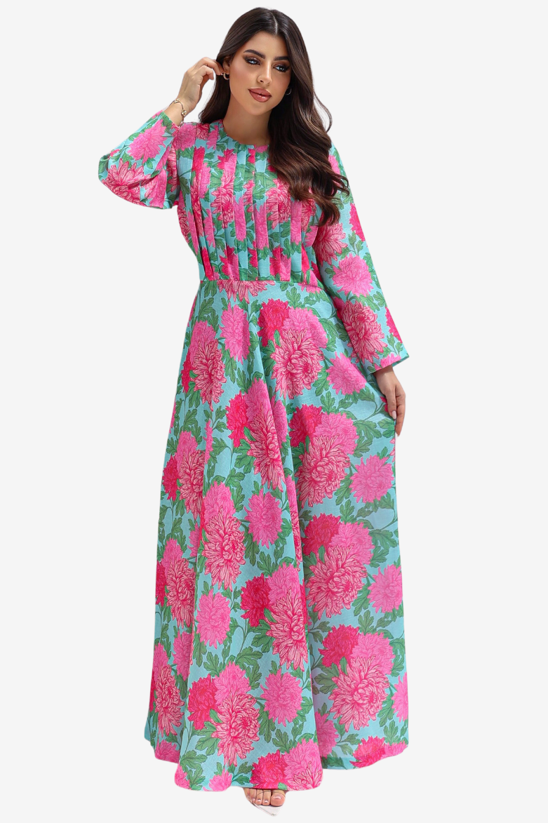 A woman modeling a long-sleeved maxi dress with a vibrant pink and green floral print on a light blue background, set against a plain light gray studio backdrop.