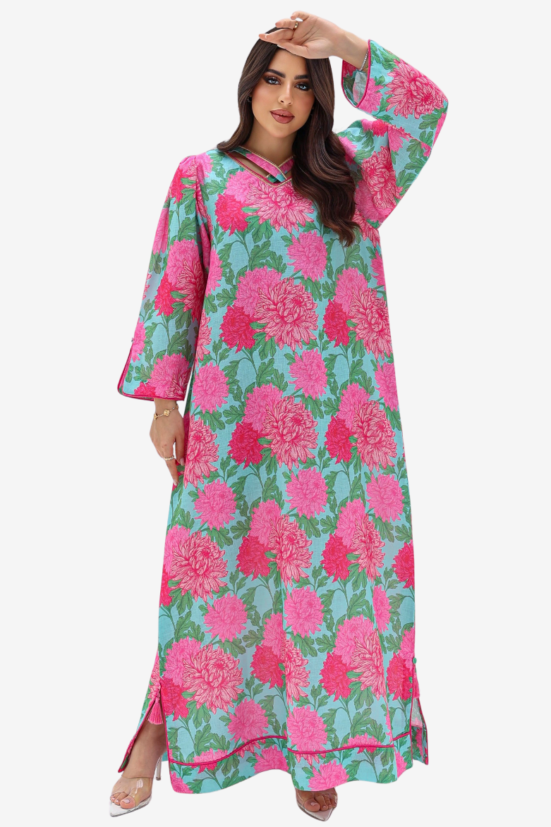 A woman modeling a long-sleeved maxi abaya dress with a vibrant pink and green floral print, set against a plain light gray background.