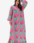 A woman modeling a long-sleeved maxi abaya dress with a vibrant pink and green floral print, set against a plain light gray background.