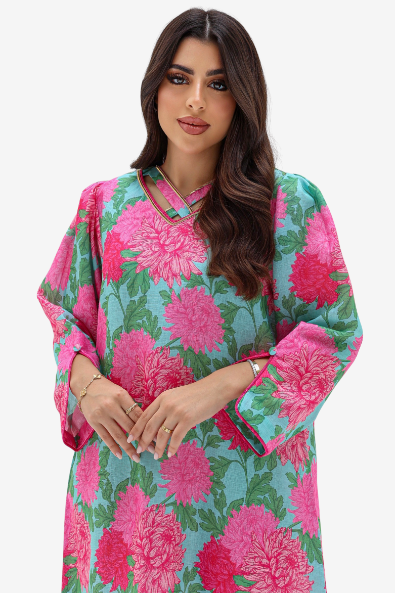 A woman modeling a light blue kaftan dress with a vibrant pink and green floral print, set against a plain light gray background.