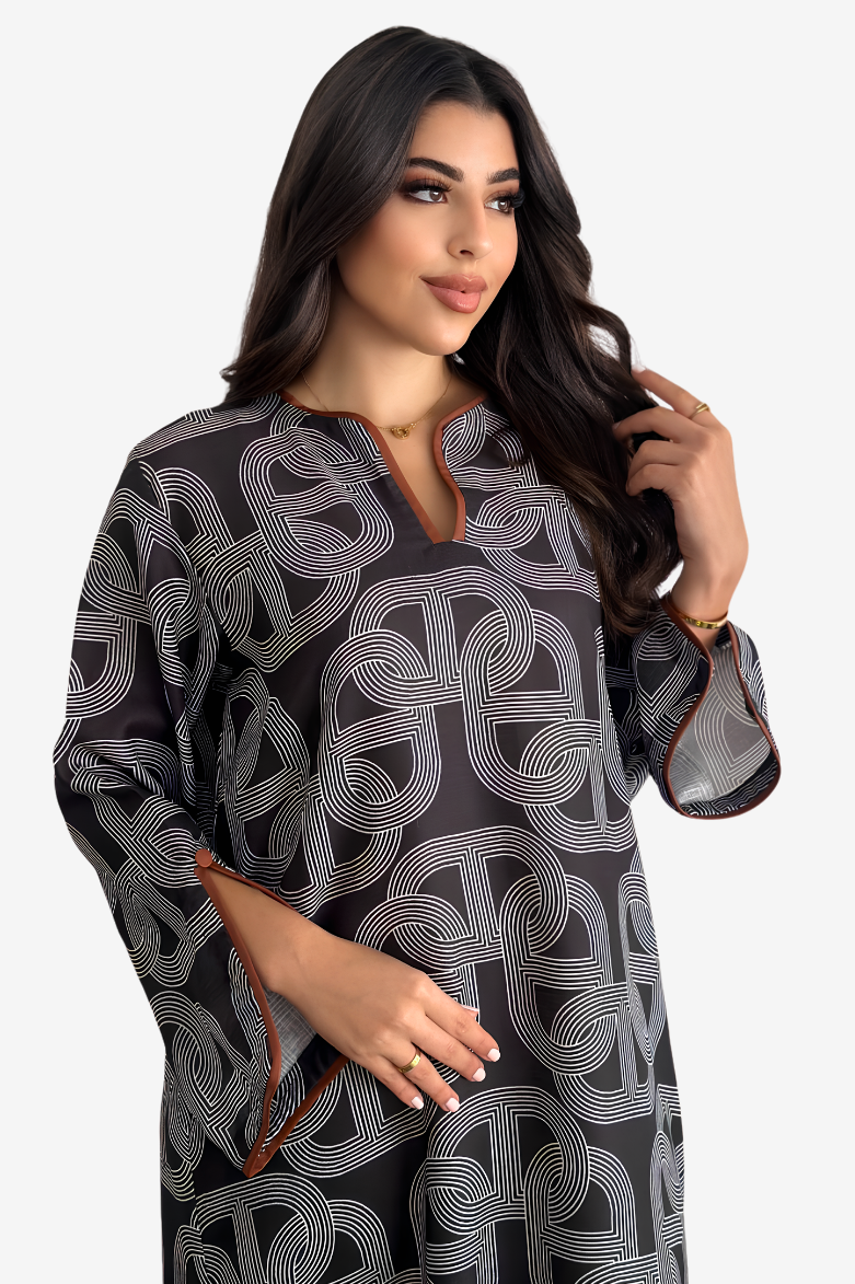A woman modeling a loose-fitting black tunic with a white geometric interlocking line pattern and a split neckline, photographed against a light gray studio background.