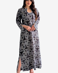 A woman modeling a long-sleeved black maxi dress with a gray geometric pattern, shown against a plain light gray background.