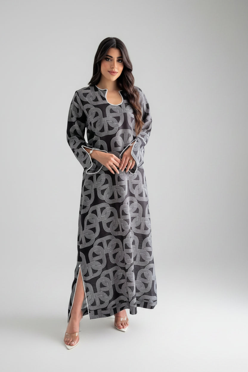 Woman in a long, patterned dress standing in a minimalistic room with a black vase.