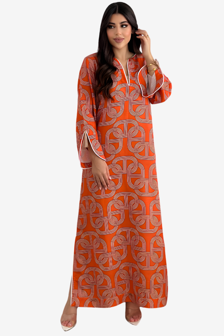 A woman modeling a long orange kaftan dress with a gray geometric pattern and white piping details, set against a plain light gray background.