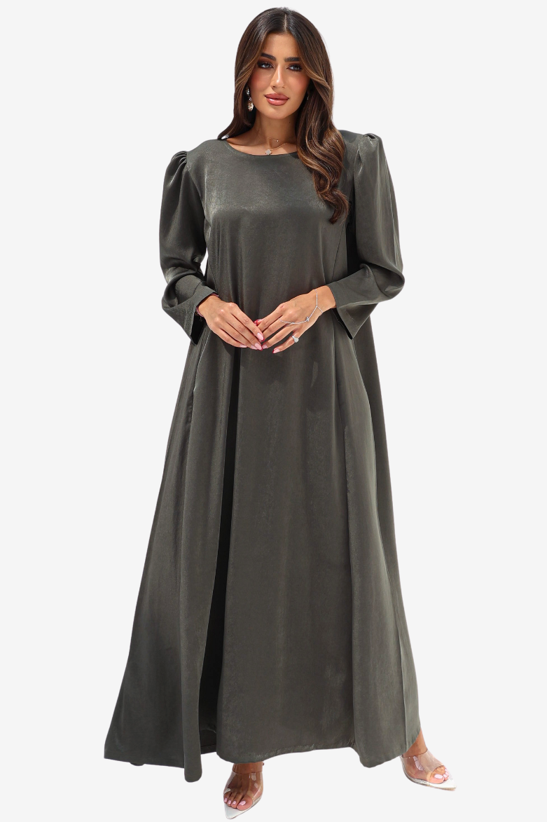 A woman modeling a long, flowing dark olive green dress with long puff sleeves and a round neckline, standing against a plain light gray background.