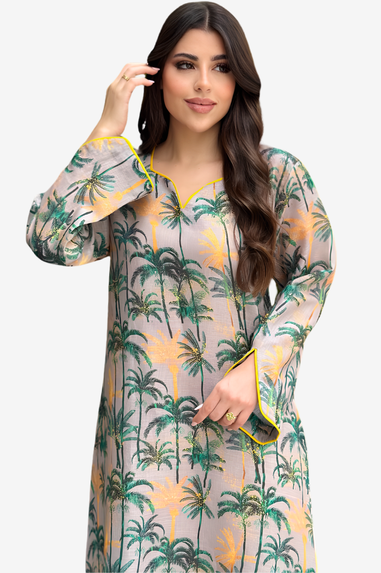 A woman modeling a long-sleeve, semi-sheer tunic dress with a green palm tree print on a light beige background with yellow accents.