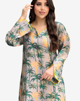 A woman modeling a long-sleeve, semi-sheer tunic dress with a green palm tree print on a light beige background with yellow accents.