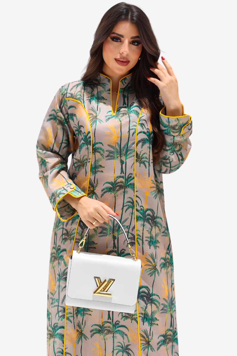 A woman modeling a long-sleeve beige kaftan dress with a green palm tree print and yellow trim, holding a white handbag with a gold LV logo.