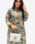 A woman modeling a long-sleeve beige kaftan dress with a green palm tree print and yellow trim, holding a white handbag with a gold LV logo.